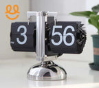 Retro black flip clock showing 3:56 PM with metallic base on white surface and plant in background