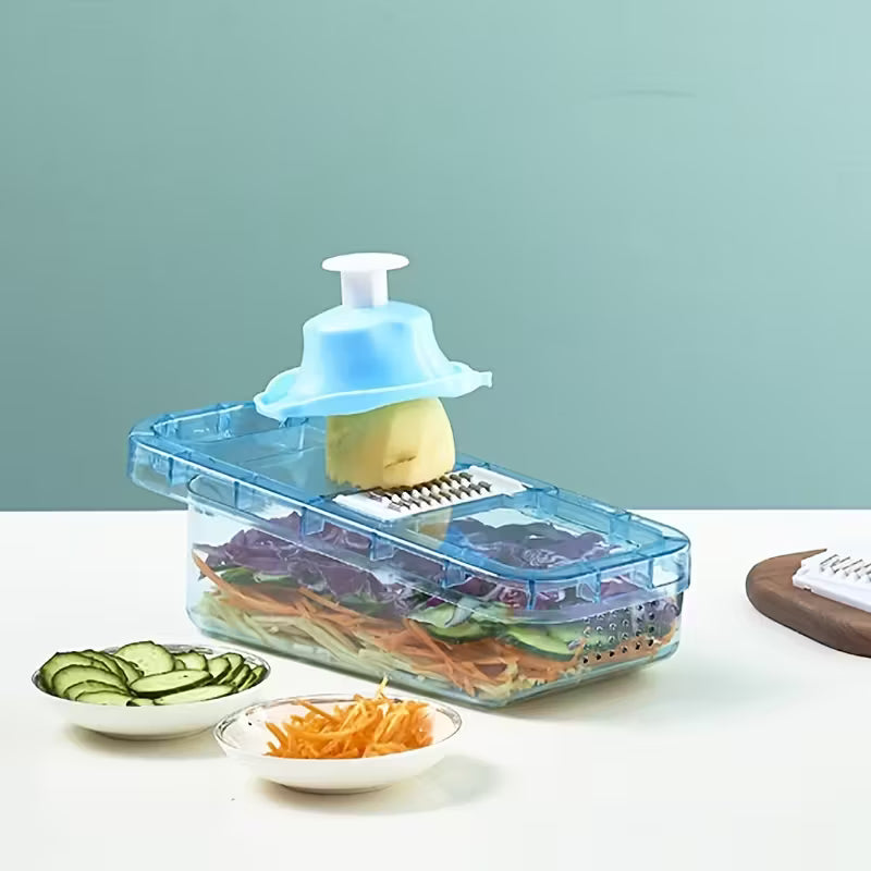 Blue plastic vegetable slicer with hand guard slicing potato over transparent container with sliced cucumbers and carrots