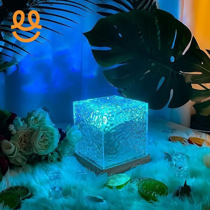 Glowing textured glass cube light on wooden base surrounded by tropical leaves, flowers, and faux ice