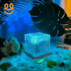Glowing textured glass cube light on wooden base surrounded by tropical leaves, flowers, and faux ice