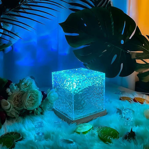 Glowing textured glass cube light on wooden base surrounded by tropical leaves, flowers, and faux ice