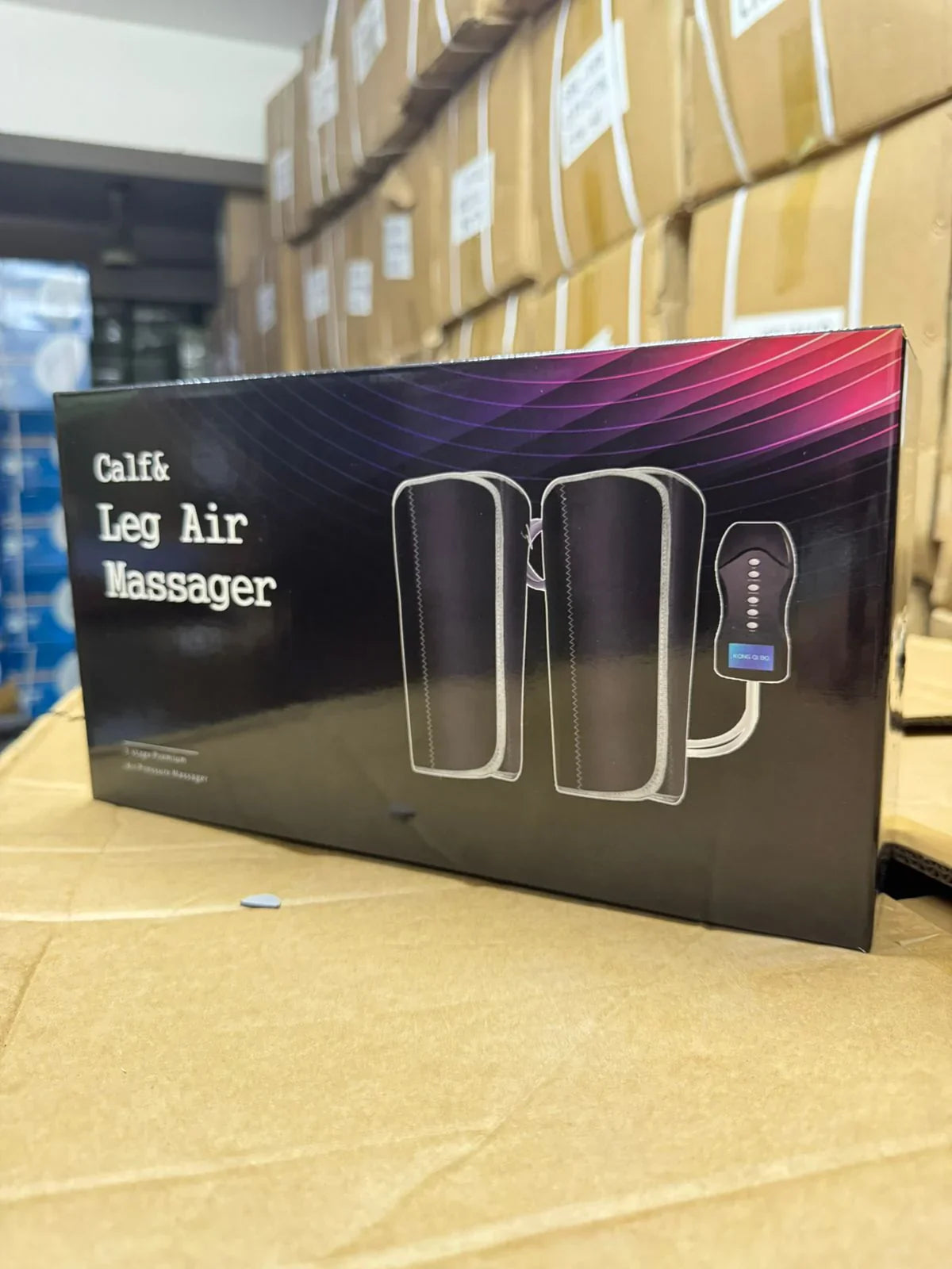 Box of Calf & Leg Air Massager with control device shown, placed on cardboard in warehouse