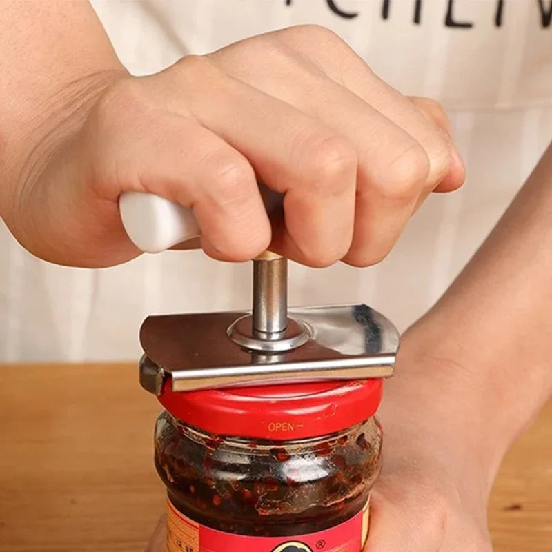 Hand using a jar opener tool to twist open a red-lidded glass jar on wooden surface