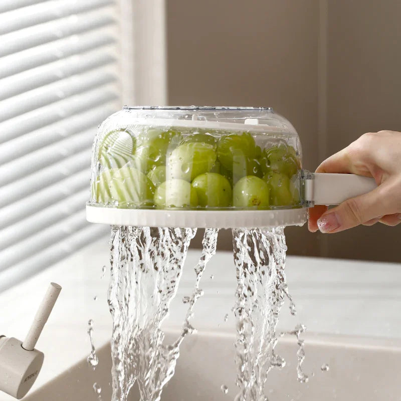 Hand holding white fruit washer draining water from green grapes over kitchen sink