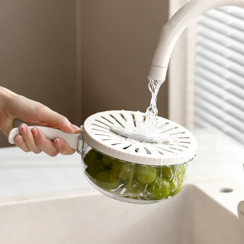 Hand holding a white strainer basket rinsing green grapes under running faucet water in a kitchen sink