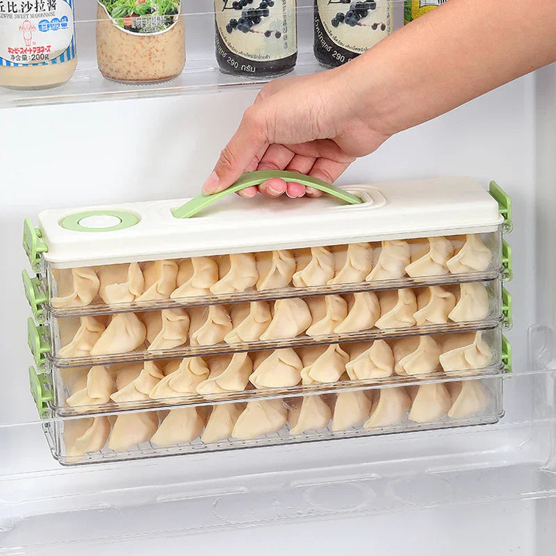 Hand lifting a three-tiered clear plastic dumpling storage box with green handles inside a refrigerator door