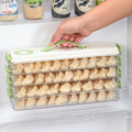 Hand lifting a three-tiered clear plastic dumpling storage box with green handles inside a refrigerator door