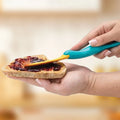 Hand spreading dark red jam on bread slice with teal and yellow spreading knife