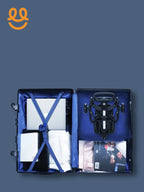Open suitcase packed with laptop, folded clothes, stroller, and magazines on blue background