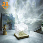 Decorative glass cube lamp emitting soft light with artistic light patterns on a tabletop with a wooden figure and framed flower poster
