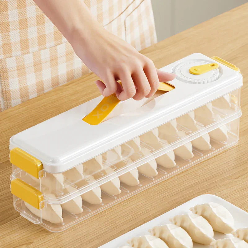 Hand holding a white and yellow plastic dumpling mold maker with two stacked trays on a wooden table